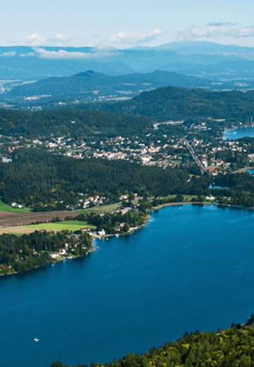 Luftaufnahme des Wörthersees in Klagenfurt, mit glitzerndem Wasser und üppiger Landschaft rundherum.