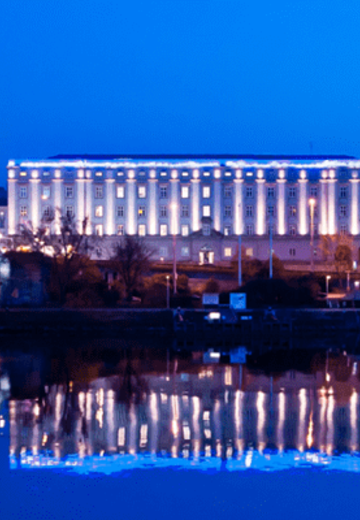 Beleuchtete Donaupromenade in Linz bei Nacht, mit reflektierenden Lichtern auf dem Wasser und stimmungsvoller Atmosphäre.
