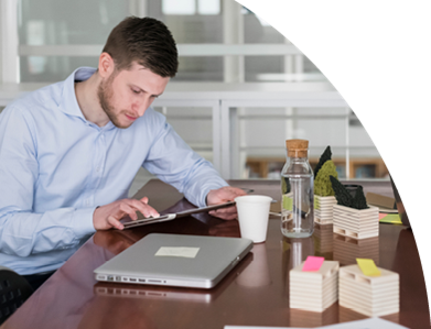 Ein Mann sitzt an einem Tisch, nutzt einen Laptop und hält einen Stift in der Hand.