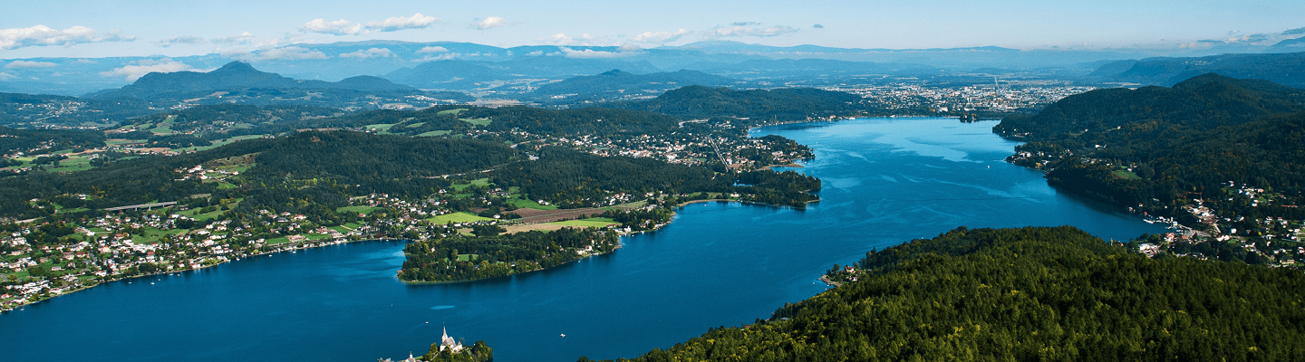 Luftaufnahme des Wörthersees in Klagenfurt, mit glitzerndem Wasser und üppiger Landschaft rundherum.